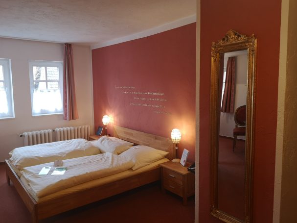 Doppelzimmer mit zwei Betten, rötlichen Wänden und großen Spiegel.