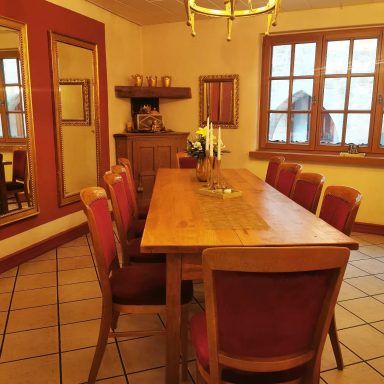 Holztisch mit roten Stühlen in einem gemütlichen Esszimmer mit großen Fenstern.